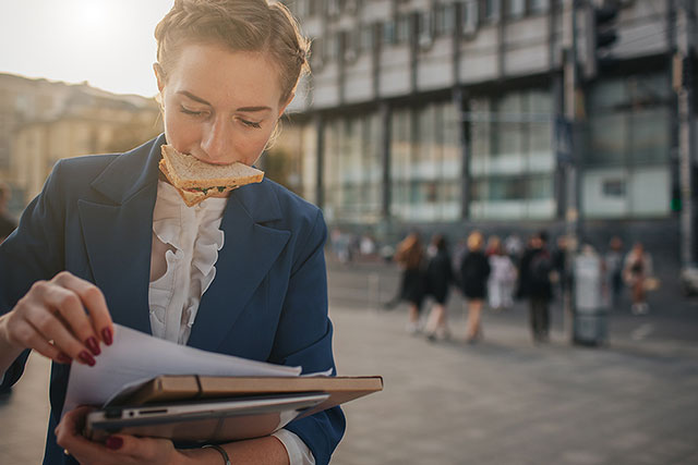 women on the street with a sandwich in her mouth and hands full