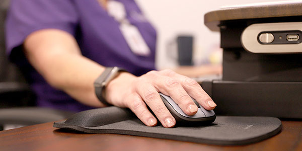 A close-up photo of a nurse's hand on a computer mouse beside computer equipment